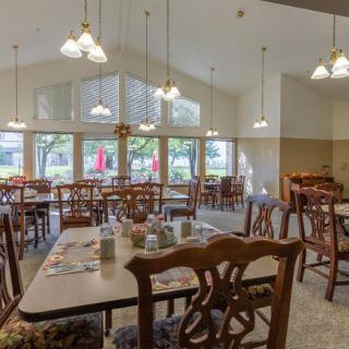An empty dining room with tables and chairs, featuring large windows and ceiling lights.