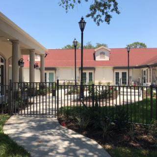 A serene outdoor space featuring a well-maintained building with a red roof, surrounded by a decorative fence and landscaped garden.