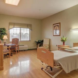 A clean and organized hospital room with a single bed, chair, table, and window.