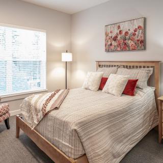 A cozy bedroom with a neatly made bed, decorative pillows, and a large window.