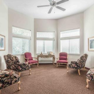 A cozy living room with armchairs arranged around a central table, surrounded by large windows and a ceiling fan overhead.