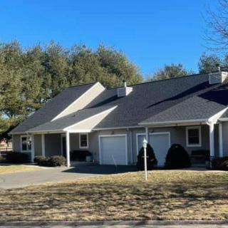A suburban residential house with a driveway and surrounding trees on a sunny day.