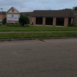 A commercial building with a visible sign, surrounded by grass and observed from the street under a cloudy sky.