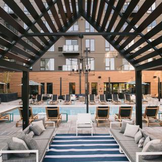 Modern outdoor seating area by a pool with an apartment building in the background.
