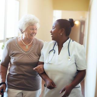 A nurse assisting an elderly woman as they walk together.