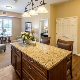 A modern kitchen featuring a granite countertop island with elegant lighting and wooden flooring.
