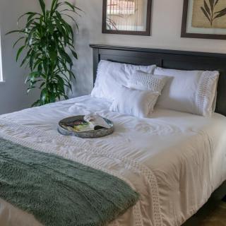 A cozy bedroom with a neatly made bed, featuring white linens, pillows, an indoor plant, and a decorative tray.