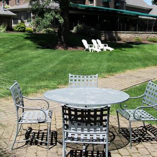 A patio set with a table and chairs on a brick surface, overlooking a lush green lawn.