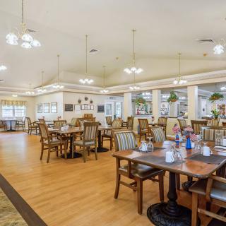 A spacious dining area with arranged tables and chairs, featuring warm lighting and a wooden floor.