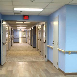 A well-lit corridor in a healthcare facility with blue walls and multiple doors leading to patient rooms.