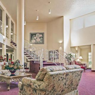 A spacious living room with elegant decor, featuring a floral sofa set, a grand staircase, and plush carpeting.