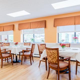 A bright and inviting dining room with orange walls, wooden flooring, and several tables and chairs arranged neatly.