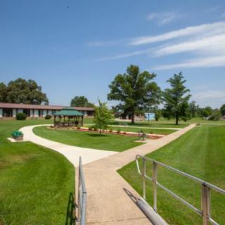 A scenic view of a park with winding walkways, manicured lawns, and trees under a clear blue sky.