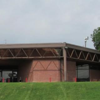 A brick building with an overhanging roof structure surrounded by a grassy lawn.