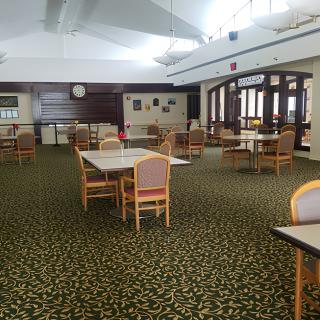An empty dining hall with arranged tables and chairs on a patterned carpet.
