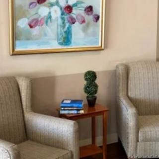 A cozy living room corner with two chairs, a small table with books, and a floral painting.