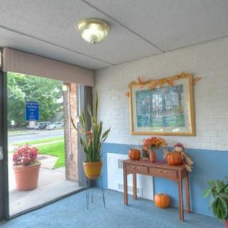 A cozy entrance decorated with autumn-themed items, including pumpkins and a potted plant by the open door.