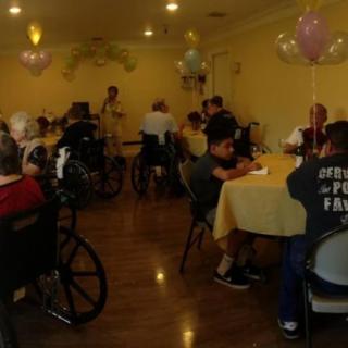 Residents gather in a nursing home dining area, participating in a social event with balloons and community interaction.