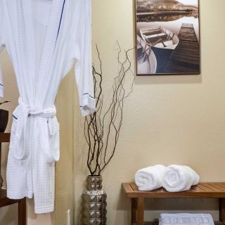 A serene spa setting with a white robe, rolled towels on a bench, and decorative elements.