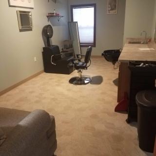 An interior view of a barbershop with a barber chair, mirror, and shelves.
