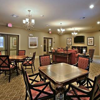 A spacious living and dining area featuring elegant chandeliers, comfortable seating, and a television.