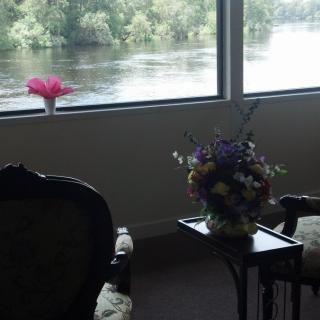 A cozy interior with a scenic river view, featuring a bouquet of flowers on a side table and comfortable seating.