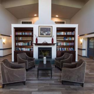 A cozy library featuring bookshelves, armchairs, and a central fireplace.