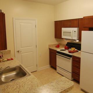 A small kitchen with wooden cabinets and standard appliances, including a stove, refrigerator, microwave, and sink.