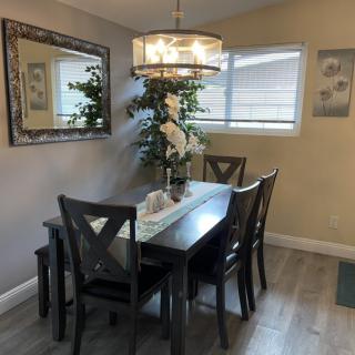 A stylish dining room with a dark wooden table and chairs, illuminated by a chandelier, featuring a large mirror and indoor plants.