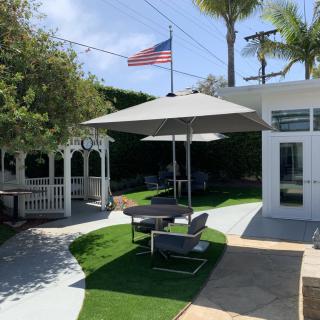 A sunny outdoor patio area featuring seating under an umbrella, with a gazebo and American flag in the background.