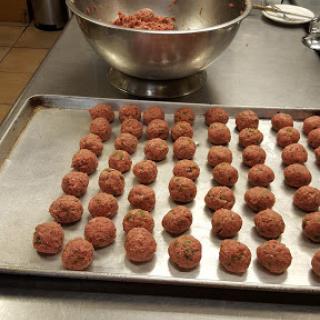 A batch of freshly rolled meatballs ready for cooking, arranged neatly on a baking tray.