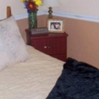 A cozy bedroom corner with a bed, nightstand adorned with flowers and a photo frame.