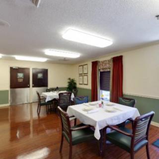 A cozy dining room with neatly arranged tables and chairs, featuring warm lighting and simple decor.