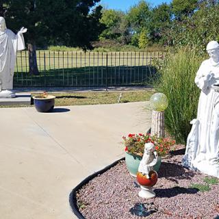 A serene garden featuring two white statues surrounded by decorative plants and stones.