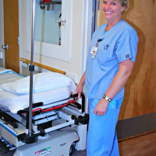 A nurse in blue scrubs standing next to a hospital gurney.