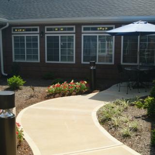 A neatly landscaped walkway leads to a building with a patio area featuring an umbrella.