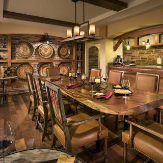 A cozy dining room with rustic decor and wooden furniture, featuring wine barrels and ambient candle lighting.