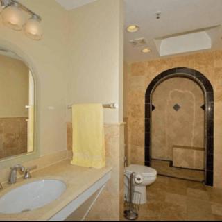A spacious bathroom featuring a sink, towel rack, toilet, and a tiled shower area with an arched entrance.
