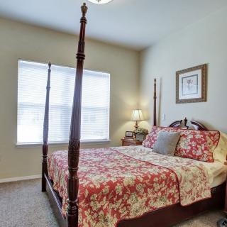 A cozy bedroom featuring a four-poster bed with floral bedding, a bedside table with a lamp, and a window with blinds.