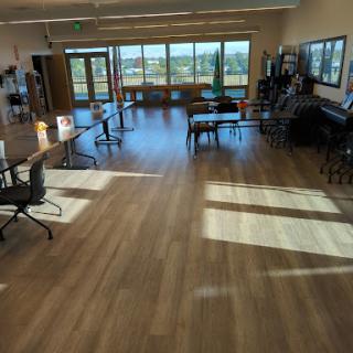 A spacious and modern office interior with ample natural light coming through large windows, featuring wooden flooring and various furniture arrangements.