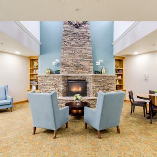 A cozy living room with a central fireplace, surrounded by modern armchairs and bookshelves.