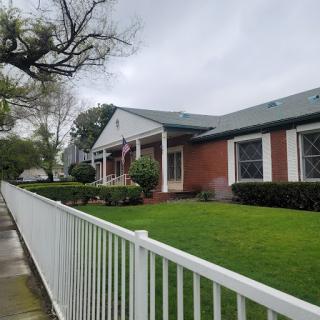 A charming brick house with a well-maintained lawn and white picket fence under a cloudy sky.