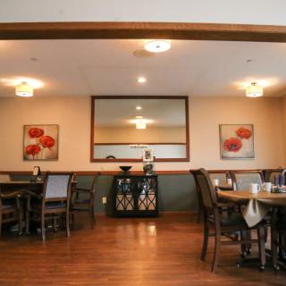 A cozy dining area with neatly arranged tables and chairs, complemented by decorative artwork and a large mirror on the wall.