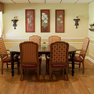 A cozy dining room with a large wooden table surrounded by six upholstered chairs, complemented by decorative wall art and sconces.