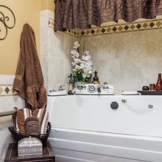 A cozy bathroom with a white tub, brown towels, decorative plants, and candles.