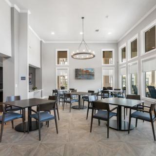 A modern dining area with tables and chairs, featuring large windows and a central lighting fixture.