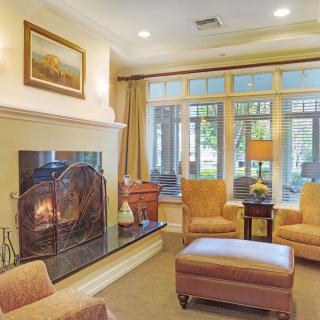 A cozy living room with a fireplace, armchairs, and large windows.