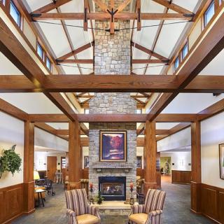 A spacious lobby with a high ceiling, featuring wooden beams and a central fireplace surrounded by chairs.