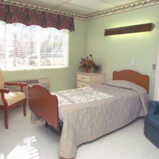 A simple, well-lit bedroom with a single bed, dresser, and chair.
