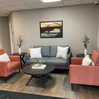 A stylish and cozy living room setup featuring a gray sofa, orange chairs, and a round coffee table, complemented by wall art.